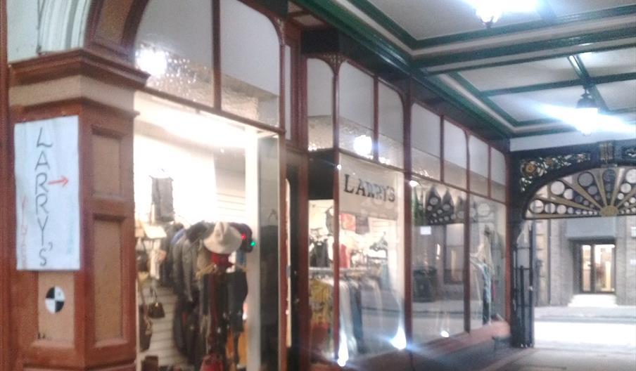 A shop display window inside a covered arcade, showing clothing, hats, and accessories. A handmade sign reading "LARRY'S" with an arrow points toward