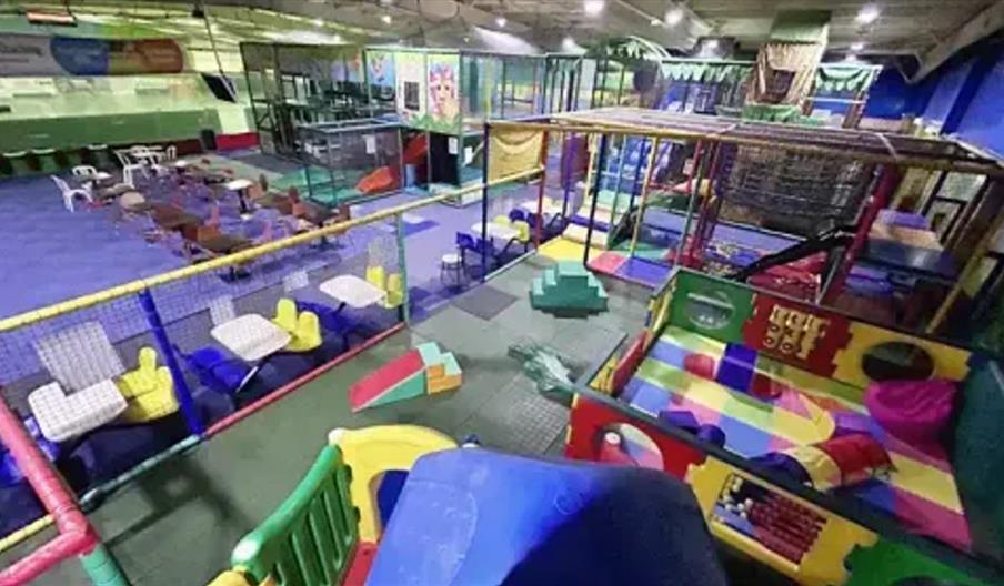 Indoor children’s play area within Little Monkeys with colourful climbing structures, slides, padded obstacles, and a fenced seating area with tables
