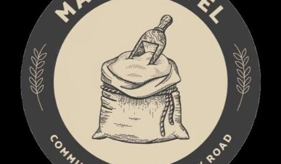 A circular logo featuring an illustration of a sack with a small shovel sticking out of it. The top of the logo reads "Malt Shovel" and the bottom say