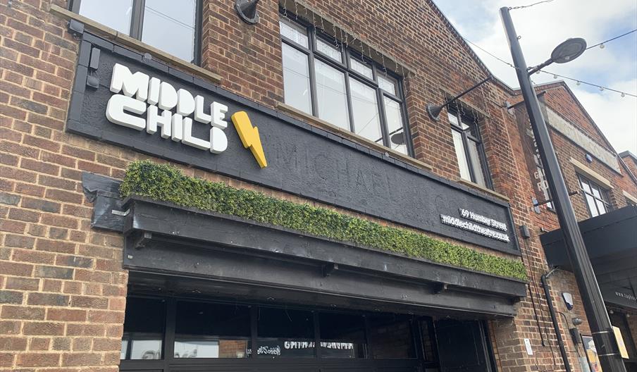 The photo shows the exterior of a brick building with a sign reading "MIDDLE CHILD" in bold white letters and a yellow lightning bolt, along with an a