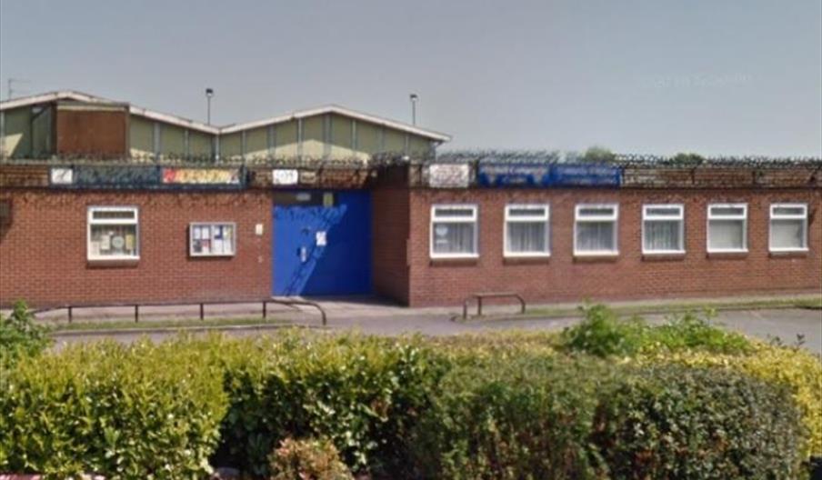 A single-story brick building with a row of small rectangular windows and a large blue door in the center, topped with fencing and barbed wire, with s