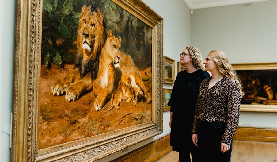 Two women looking at a painting of a family of lions in an art gallery