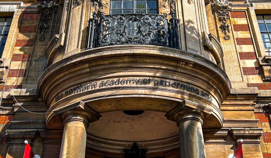 Close-up view of the entrance to NAPA, a historic building with two large columns, ornate architectural details, and the sign "the northern academy of