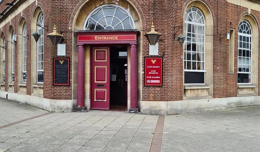The image shows the entrance of a brick building called "The New Griffin," featuring large arched windows, a red double door with pink columns, and si