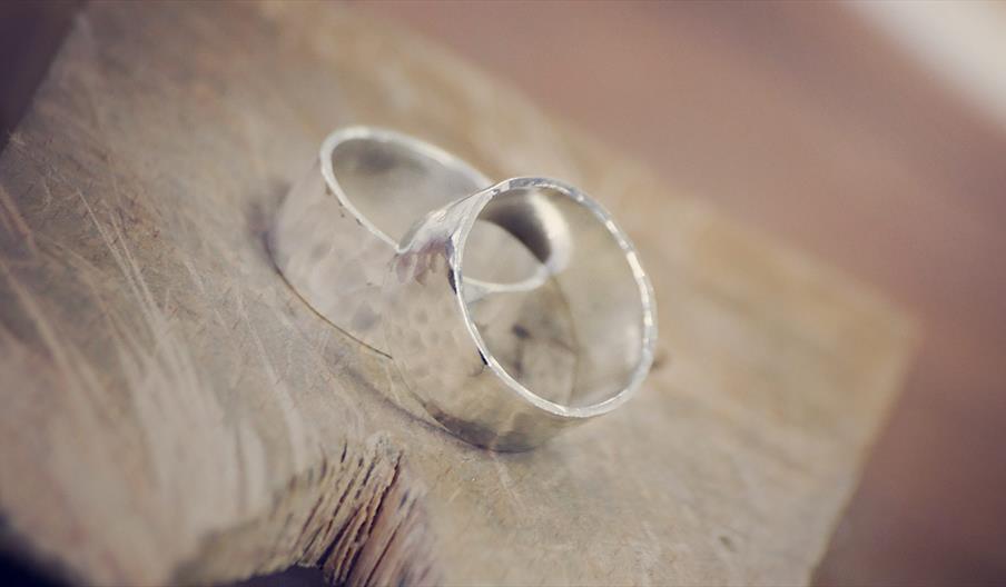 Two silver wedding bands with a hammered texture are placed together on a rough wooden surface.