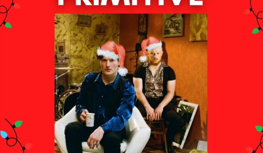 A promotional poster with a red background and Christmas light decorations features two men wearing Santa hats, sitting in a vintage-styled room with
