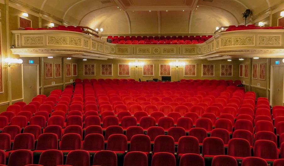 Empty theatre auditorium featuring rows of red seats, ornate balcony boxes on both sides, and decorative gold detailing on the walls and ceiling at Pa