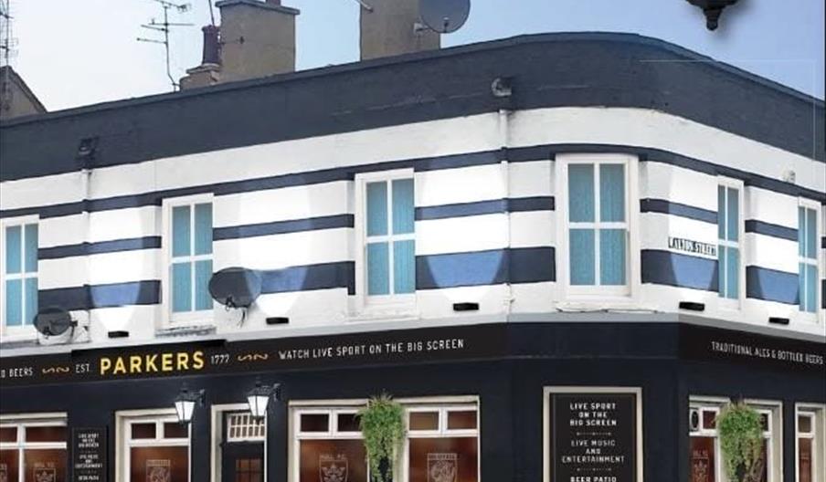 A corner pub called Parkers, painted with bold black and white horizontal stripes, features large windows, hanging lantern-style lights, and potted pl