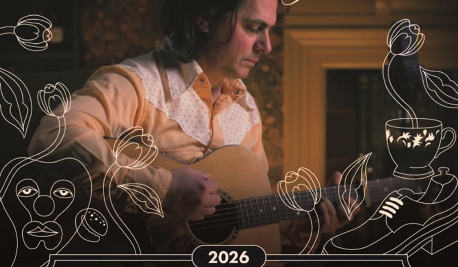 Poster for "Pink Moon Rising: A Nick Drake Tribute by Alex Lewis" showing a man playing an acoustic guitar in a warm, dimly lit room, surrounded by ar