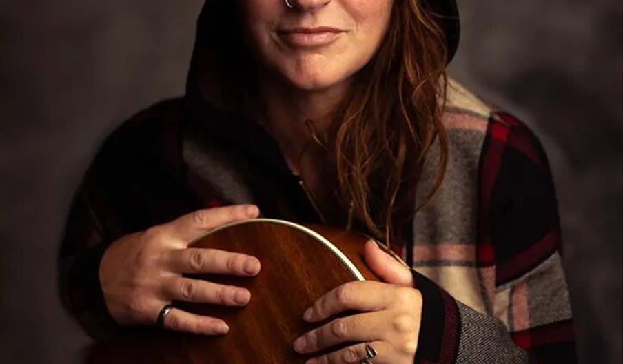 A promotional poster featuring musician Ruth Theodore, shown in a plaid hoodie holding a guitar, with event details for her full band tour at The New