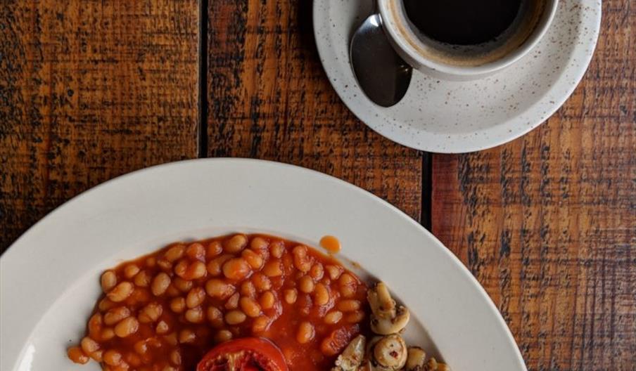 A cup of coffee and a full english breakfast from above on a wooden table.