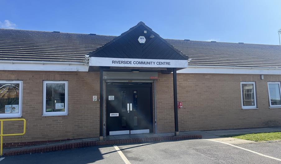Single-story brick building with a sign above the entrance reading "Riverside Community Centre," featuring double doors and multiple windows on either