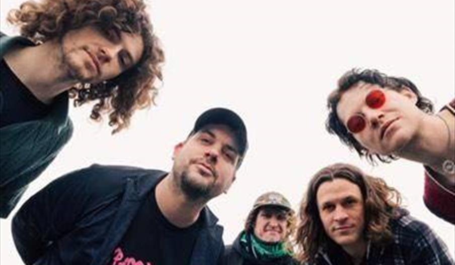 Five people with varying hair styles, some with curly hair and one wearing a cap, are standing close together and leaning toward the camera, which is