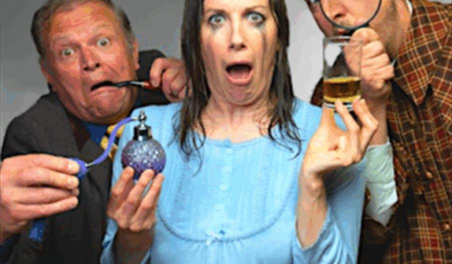 Three people posing with exaggerated shocked and curious expressions; a woman in the centre holds a spray bottle and a glass, while the man on the lef