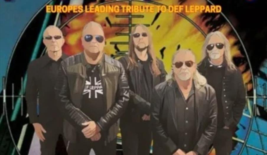 Five men in black clothing and sunglasses stand in front of a colorful, geometric background, with bold yellow and orange text above them reading "SHE