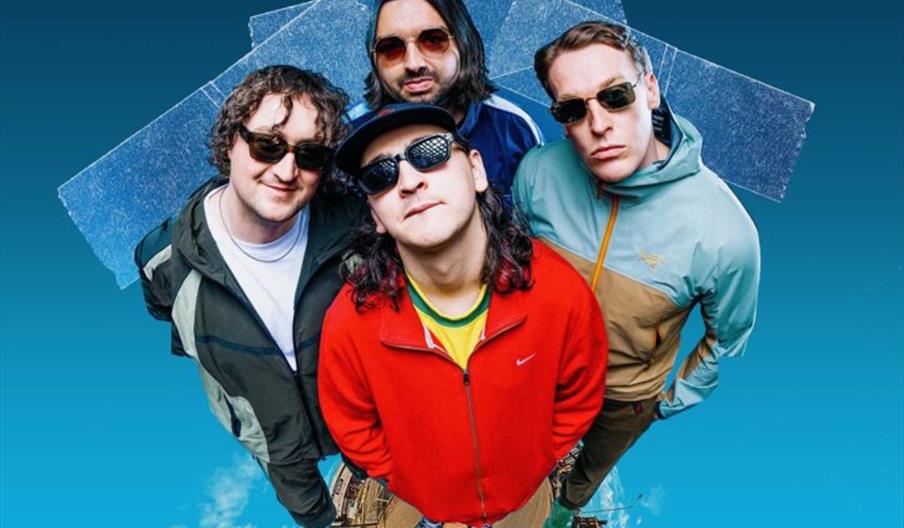 Poster for a concert by The Cheap Thrills, featuring a fisheye photo of four band members wearing sunglasses and colorful jackets, with event details