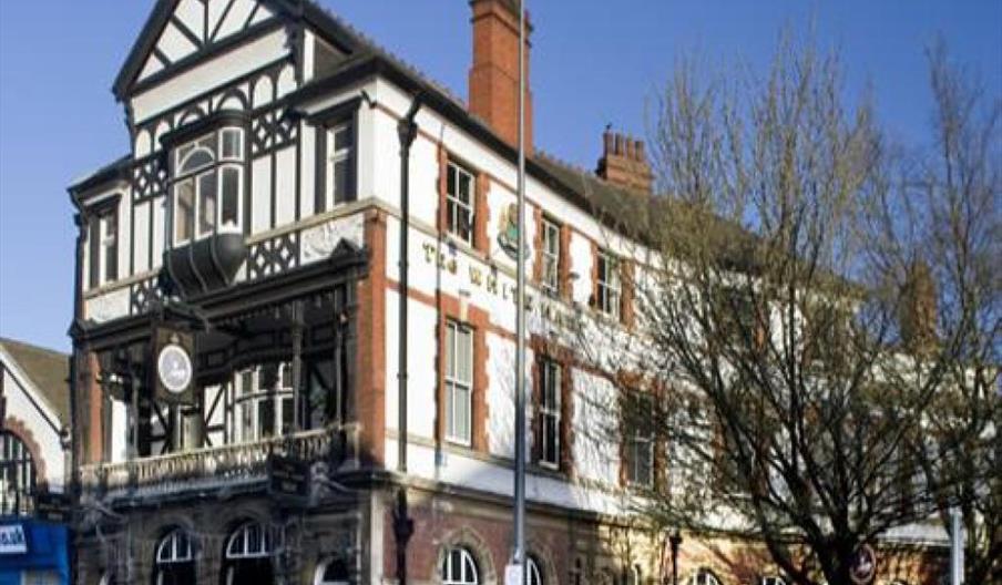A large, old-fashioned building, The White Hart with Tudor-style black and white timber framing on the upper floors and red brick on the ground level,