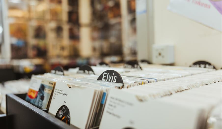 A close-up view of vinyl records organized in bins at a record store, with a divider labeled "Elvis" prominently displayed among the albums.