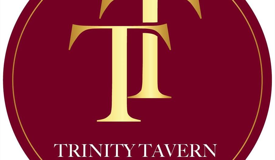 A circular logo with a maroon background and gold border featuring large, overlapping gold letters "TT" in the centre. Below the letters, the text rea