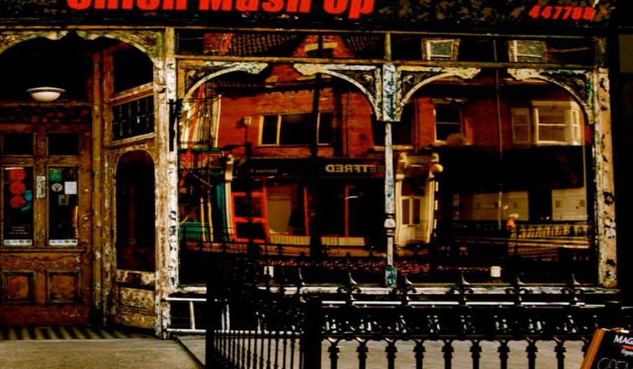 Exterior of "Union Mash Up," a venue with a vintage storefront featuring large windows reflecting the street, a decorative iron fence, and a chalkboar