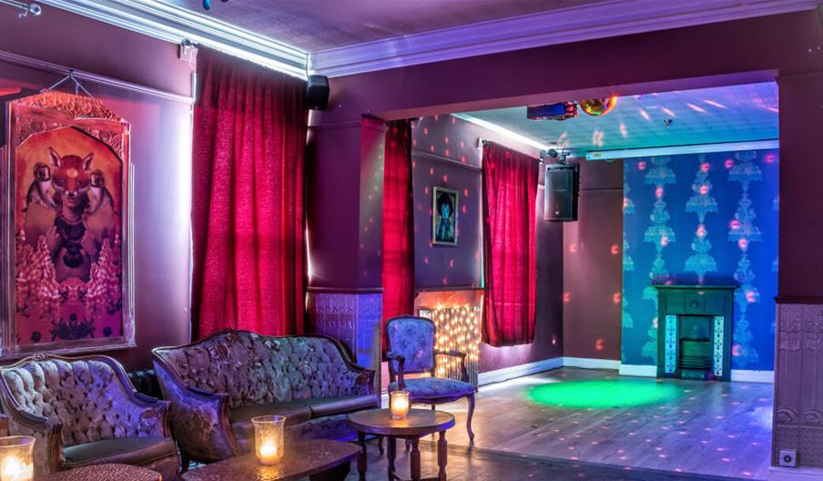 Union Mash Up interior with vintage sofas and armchairs, small tables holding glowing candles, vibrant red curtains, and moody colored lighting. A lar