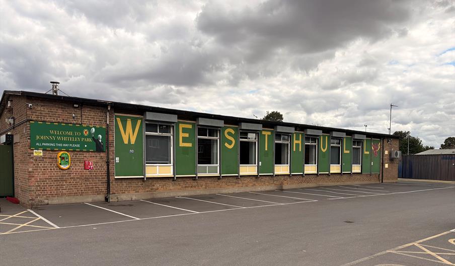 The exterior of West Hull Community Centre, an old brick bungalow with green walls and yellow letters on each that spell out 'West Hull'.