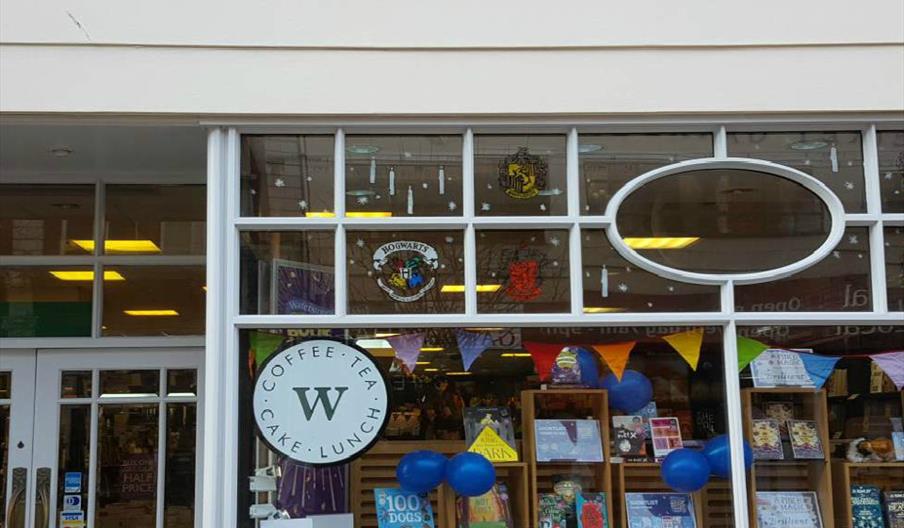 The storefront of  Waterstones bookshop Hull, decorated with Harry Potter-themed banners, house crests on the windows, blue balloons, and books displa