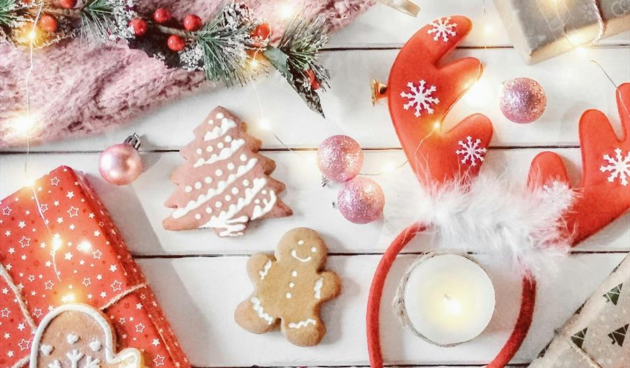 A festive flat lay featuring wrapped Christmas gifts, decorated cookies shaped like a mitten, tree, and gingerbread person, red reindeer antler headba