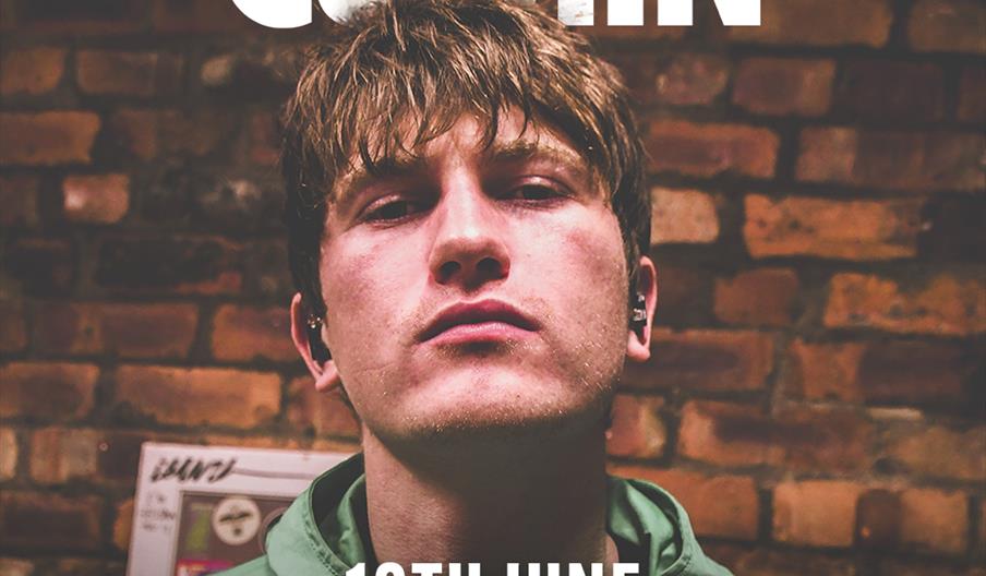 A promotional poster featuring a young man in a green jacket standing in front of a brick wall, with bold text above and across him reading "Andrew Cu