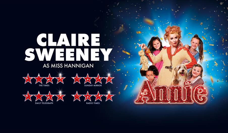 Promotional image for the musical "Annie," featuring Claire Sweeney as Miss Hannigan surrounded by four children and a dog, with the name "Annie" in g
