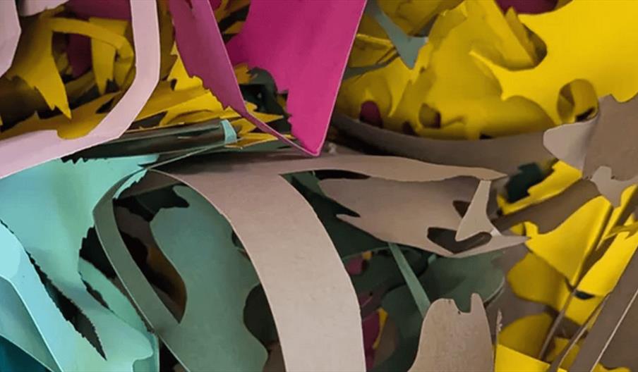 A close-up view of various colorful pieces of paper, including yellow, pink, teal, and brown, intricately cut and layered in an abstract, overlapping