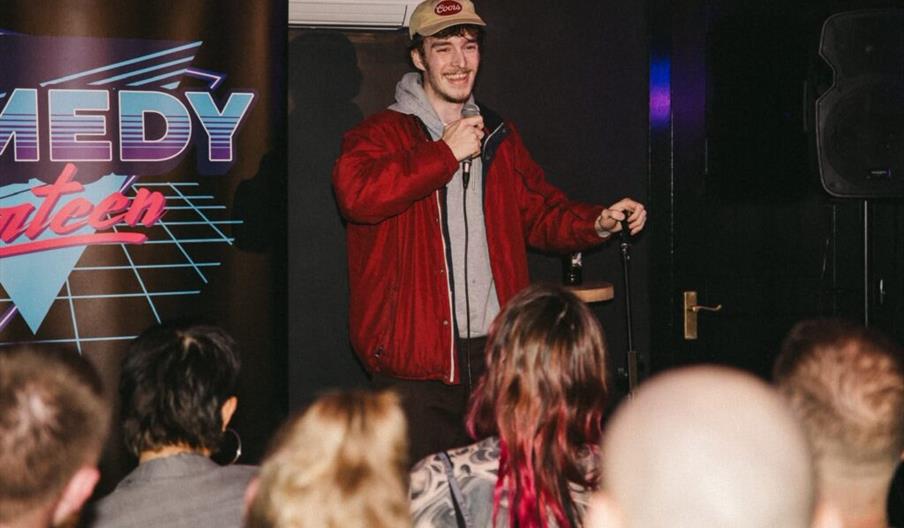 A man stands at the front of a crowd performing standup.