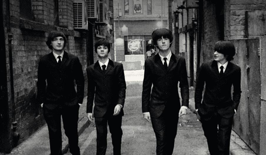Black and white promotional poster showing four men in suits walking down an alley, styled to look like The Beatles, with large text reading "Beatles