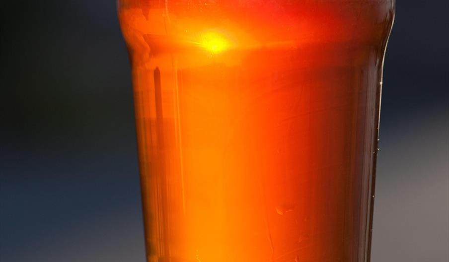 A pint of beer sits on a wooden surface with the sun shining through it.