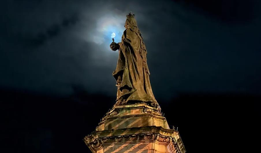 A statue of Queen Victoria at night, shot as though she was holding the moon.