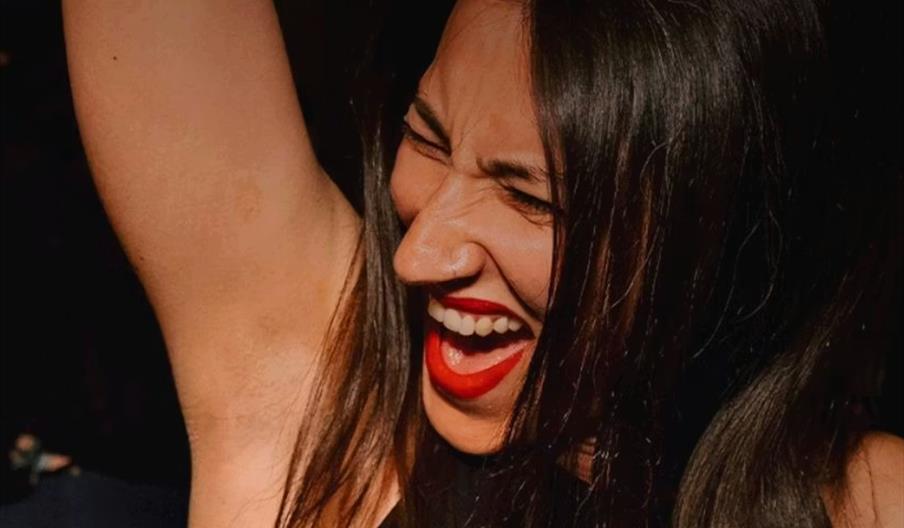 A woman with long dark hair and bright red lipstick is smiling widely with her eyes closed and one arm raised in excitement; the word "BEYOND" in bold