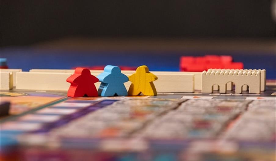 Three small game pieces in red, blue, and yellow stand next to each other on a colorful board game, with white game board structures in the background