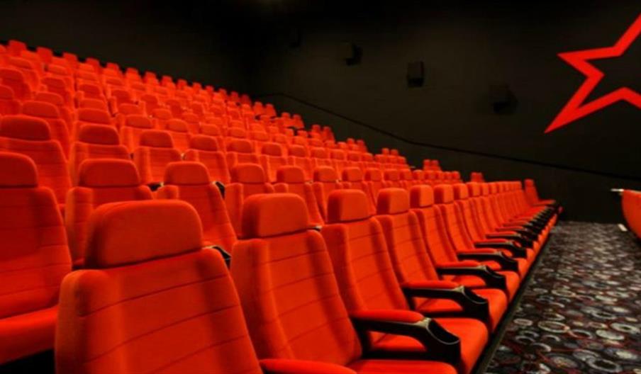 Rows of empty, bright red theater seats face a dark wall decorated with a large, outlined red star; the floor has a patterned carpet.