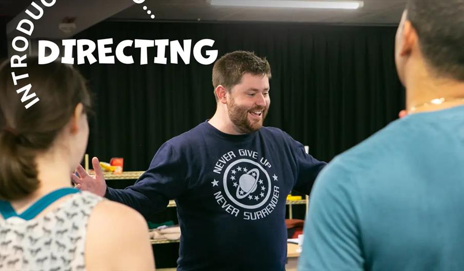A man smiling and gesturing with open arms is talking to two people whose backs are to the camera, with the words "Introducing... Directing" overlaid