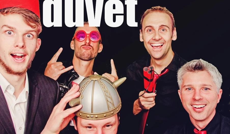Five smiling men pose playfully in costumes and accessories in front of a black background with large white text that reads "the ultimate covers band!