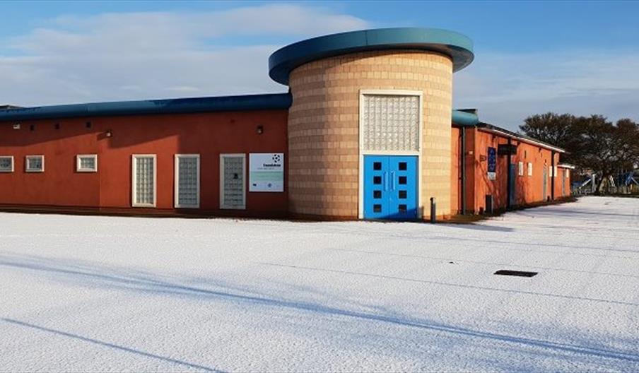 Single-story building with a distinctive round entrance and bright blue doors, identified as the Eastmount Community Centre, surrounded by a snow-cove