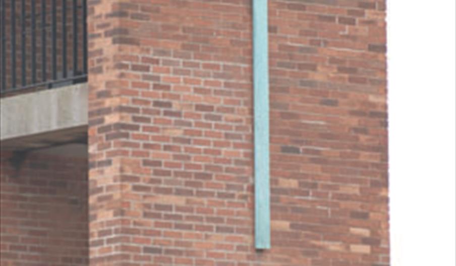 Brick exterior wall of the Danish Church in Hull, featuring a large pale green cross mounted vertically on the red brick facade.