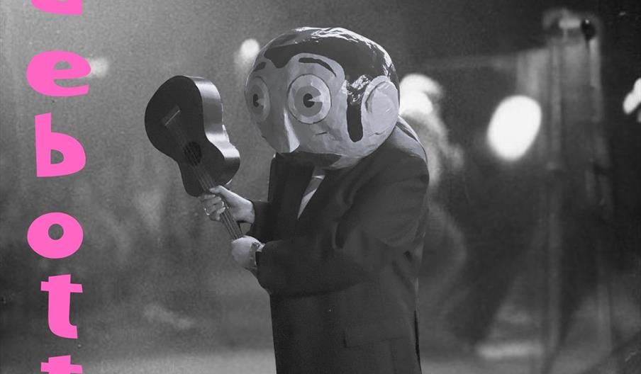 A promotional poster featuring a person in a suit with a large papier-mâché head holding a guitar onstage, with the text "Frank Sidebottom Calling" in