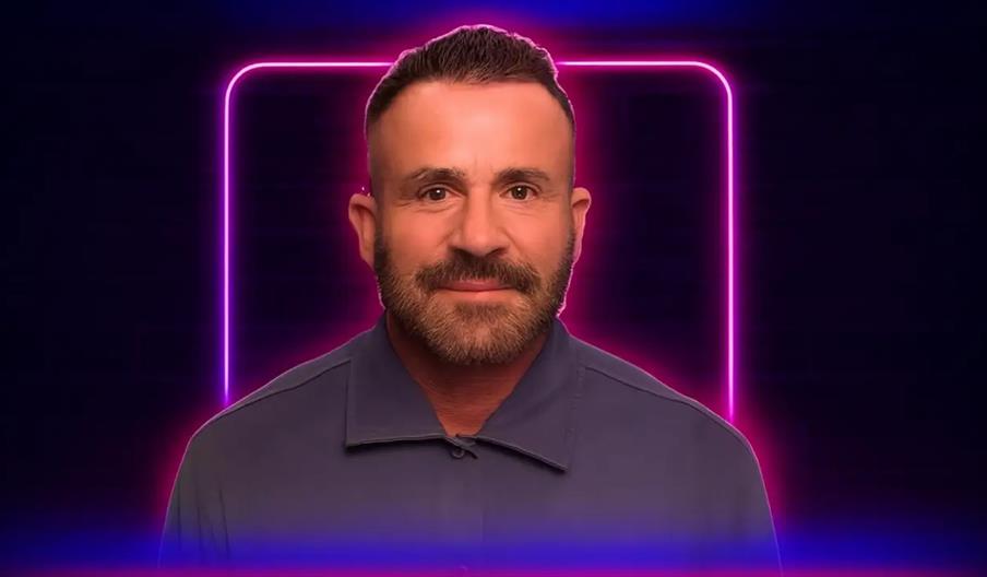 A man with short dark hair and a trimmed beard is smiling slightly, standing in front of a glowing neon pink square on a dark background.
