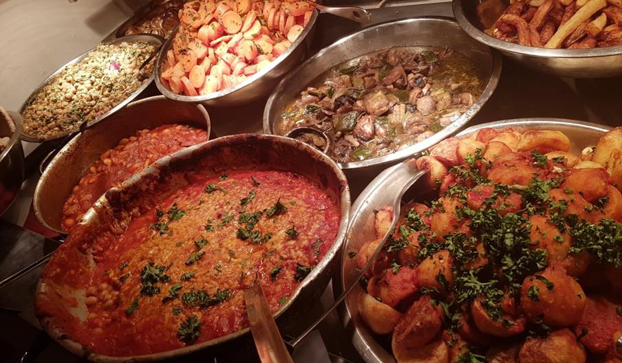 An assortment of metal bowls with different vegetarian dishes, such as soups, potatoes, chips, mushrooms and carrots.