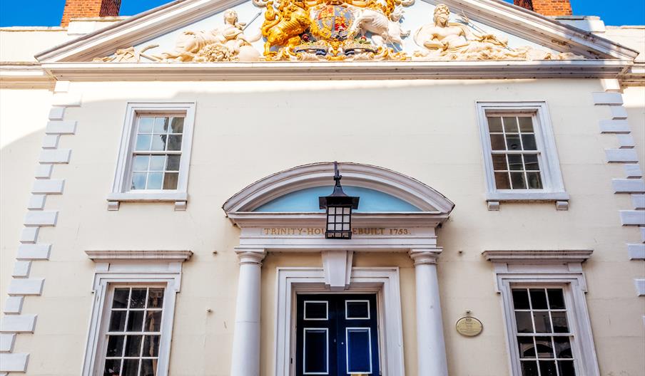 Front view of Hull Trinity House, showing its symmetrical facade with white walls, a central blue door framed by columns, and large sash windows on ei