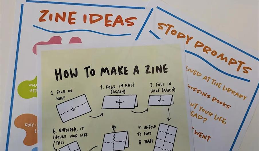 Three colourful handouts are stacked on a table; the top one shows step-by-step illustrated instructions titled "How to Make a Zine," while the others