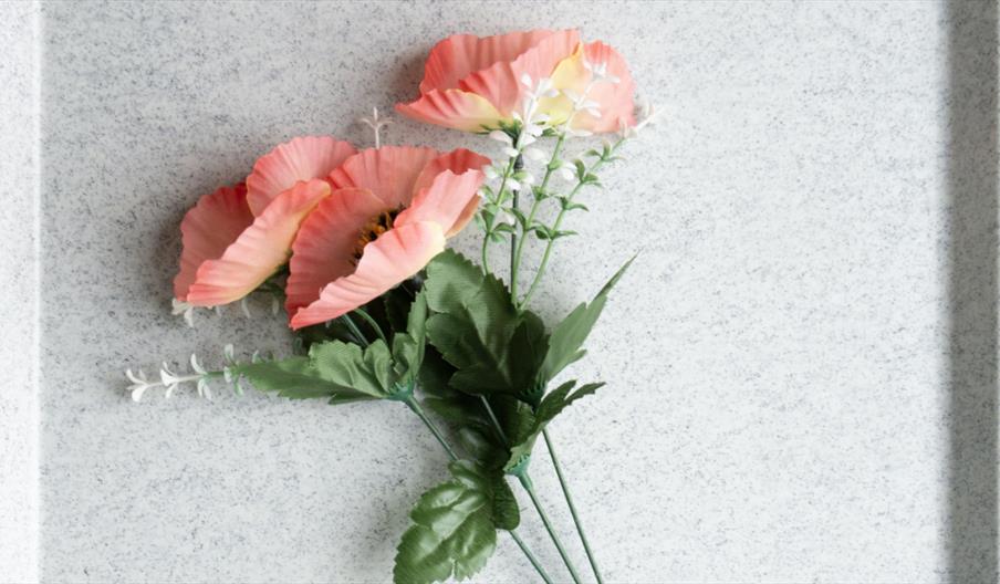 A small bouquet of artificial pink flowers with green leaves is arranged on a speckled gray tray.
