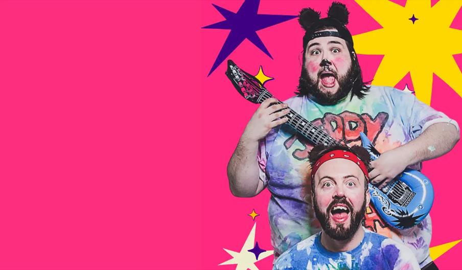 Two men in colorful tie-dye shirts pose enthusiastically against a bright pink background with large, playful star shapes; one man wears fuzzy bear ea