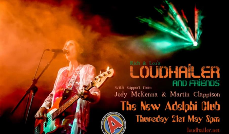 A musician plays an electric guitar and sings into a microphone on stage, surrounded by vibrant orange and green stage lighting and smoke, with event